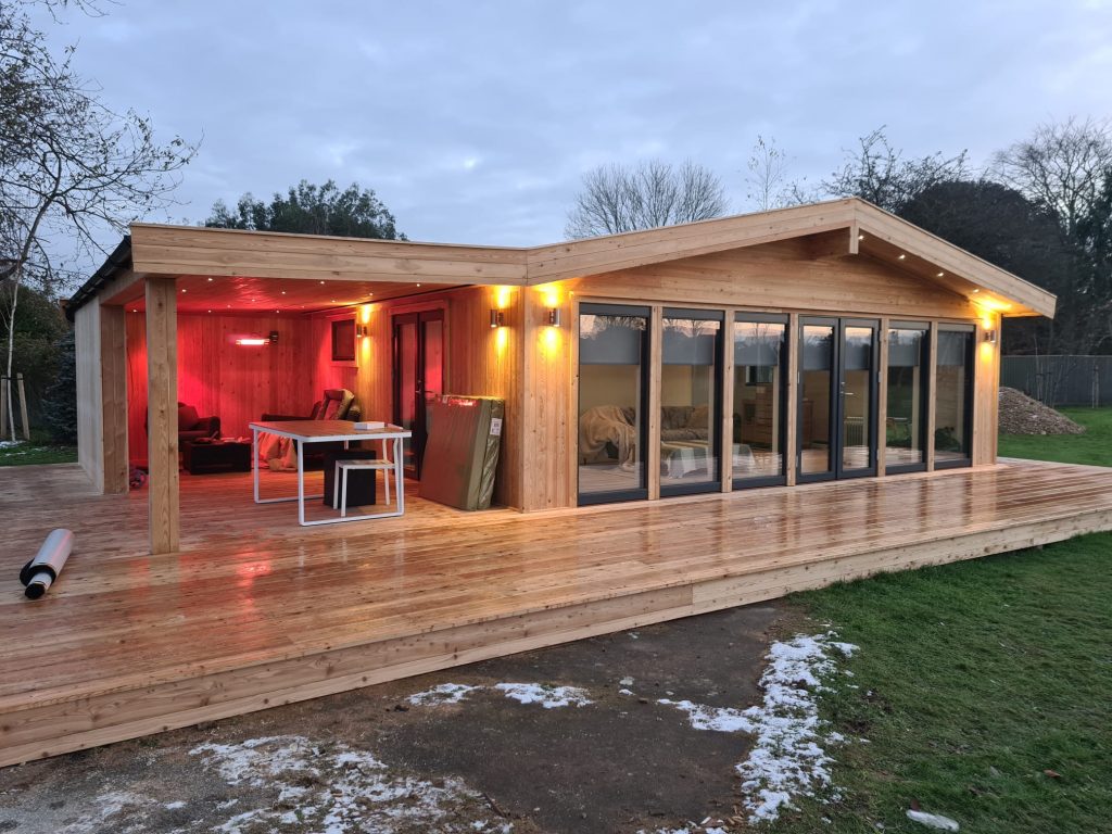 Large timber building in a garden with large decking around to provide an outside snug seating area. Lots of lights set in the roof provide a cozy area for use all year round.