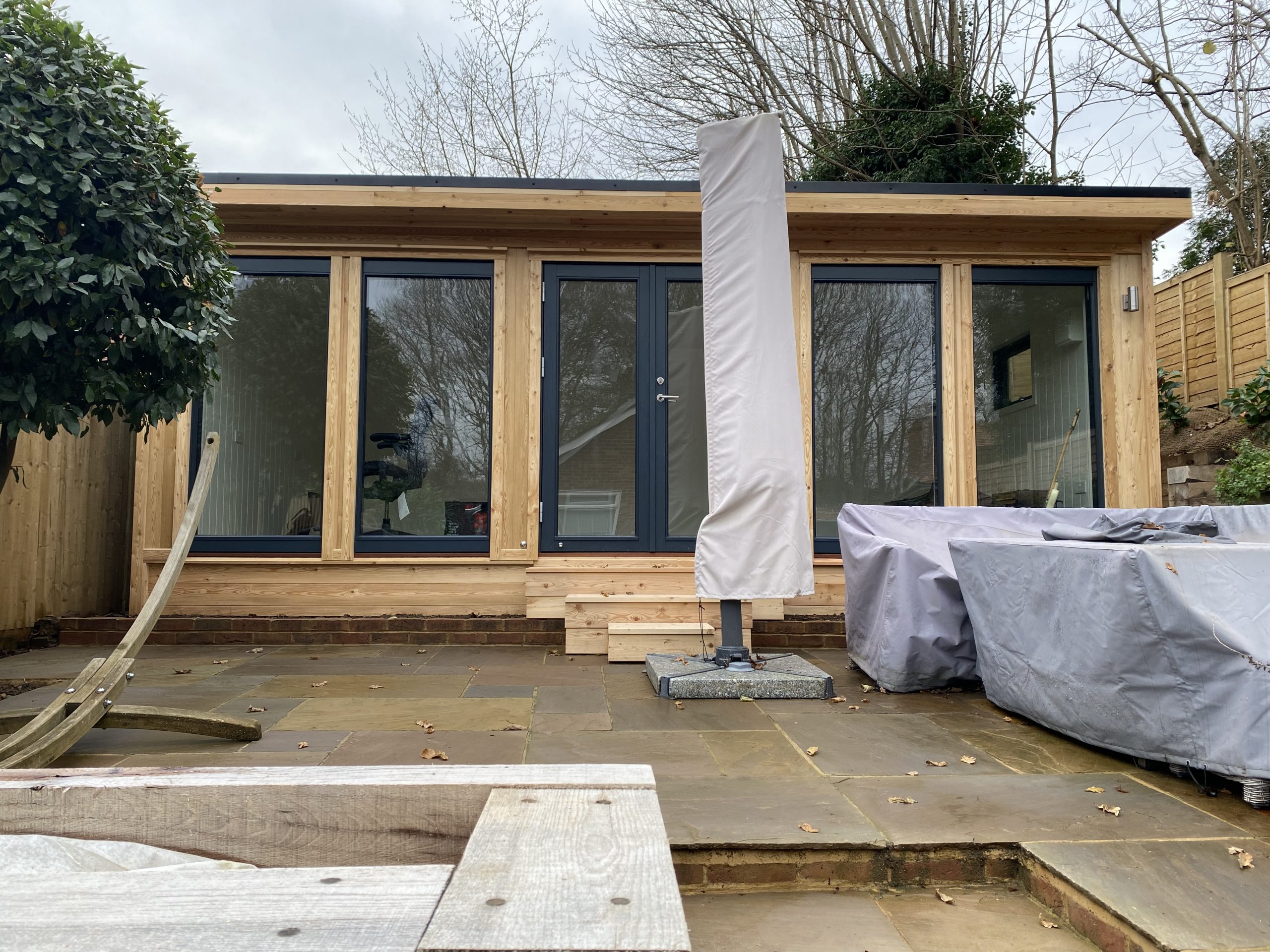 Insulated garden room made of quality timber featuring a front wall of windows and glass doors.