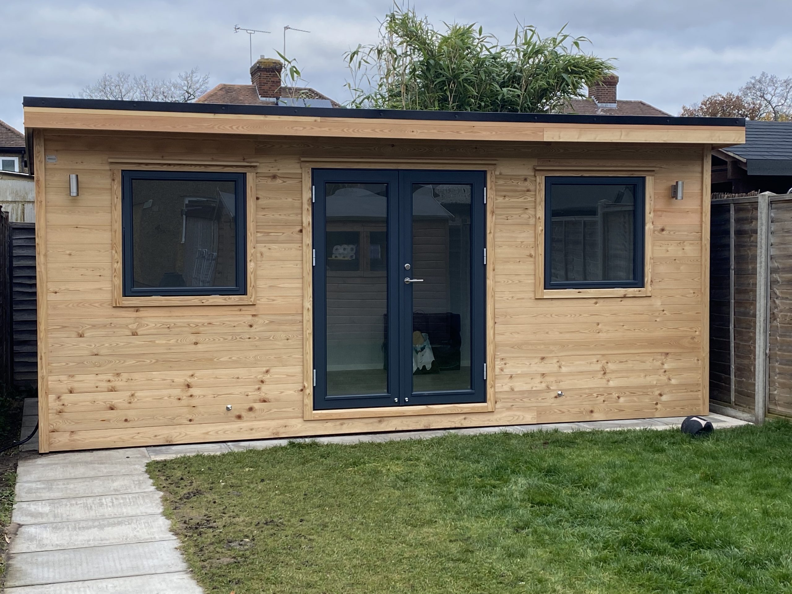 Wooden garden building with insulation that is in a small garden. Featuring double doors and two windows.